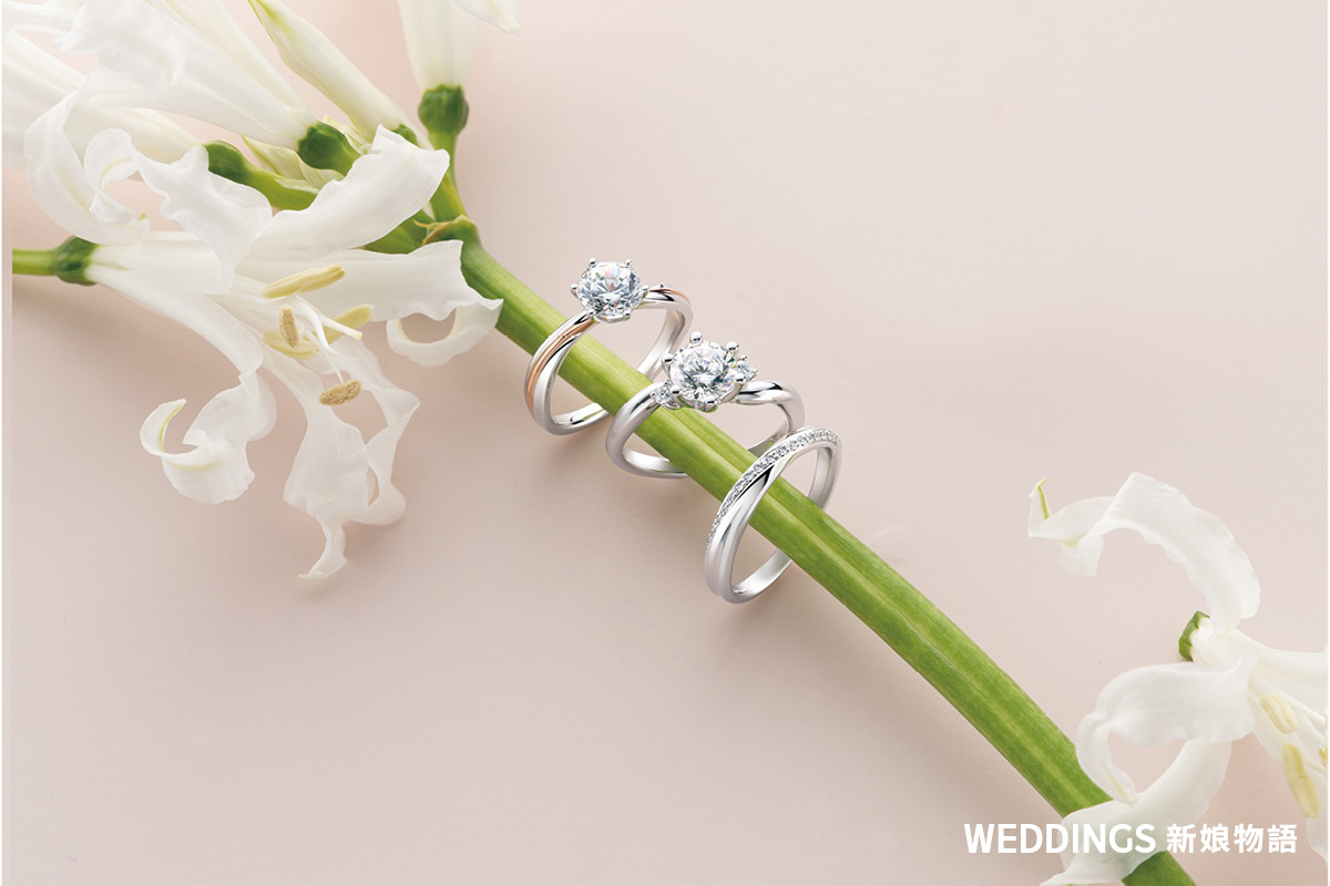 ALUXE 亞立詩精緻鑽戒與結婚對戒搭配白色花卉點綴,展示婚戒設計細節與金屬質感